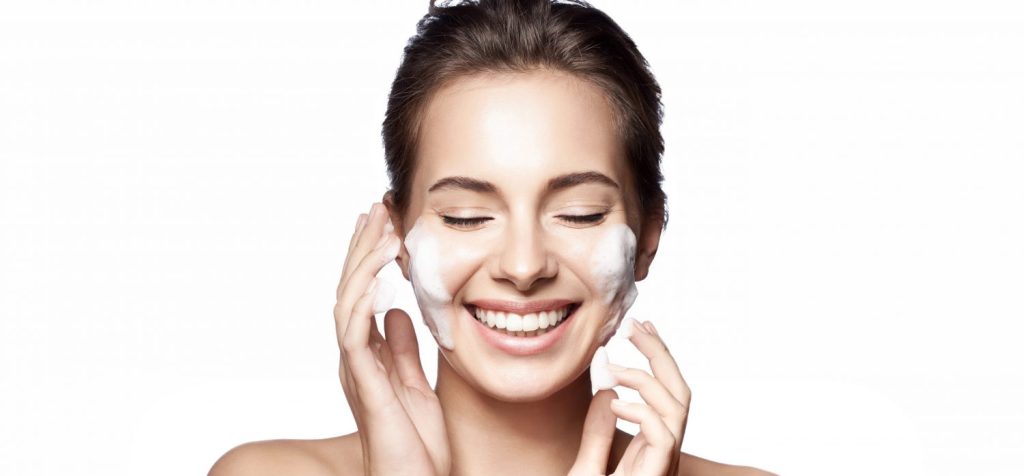 Smiling woman with perfect skin hair back with foam cleanser on her face.