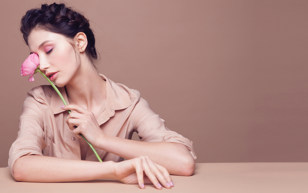 Brunette woman with braided hair holds a tulip against a pink background.