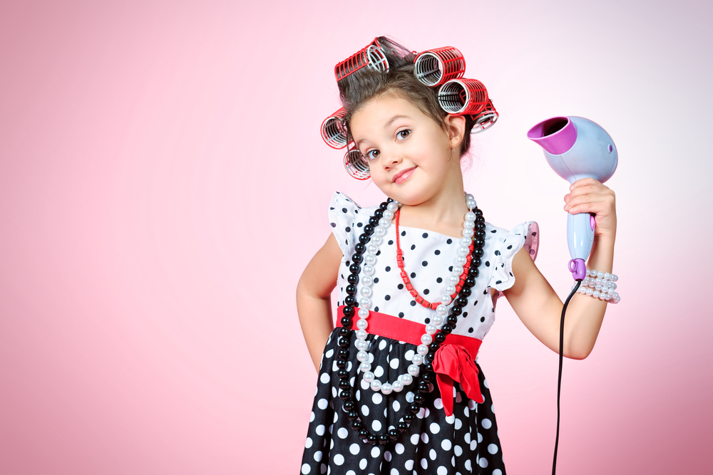 little girl with curlers in her hair holding a hairdryer