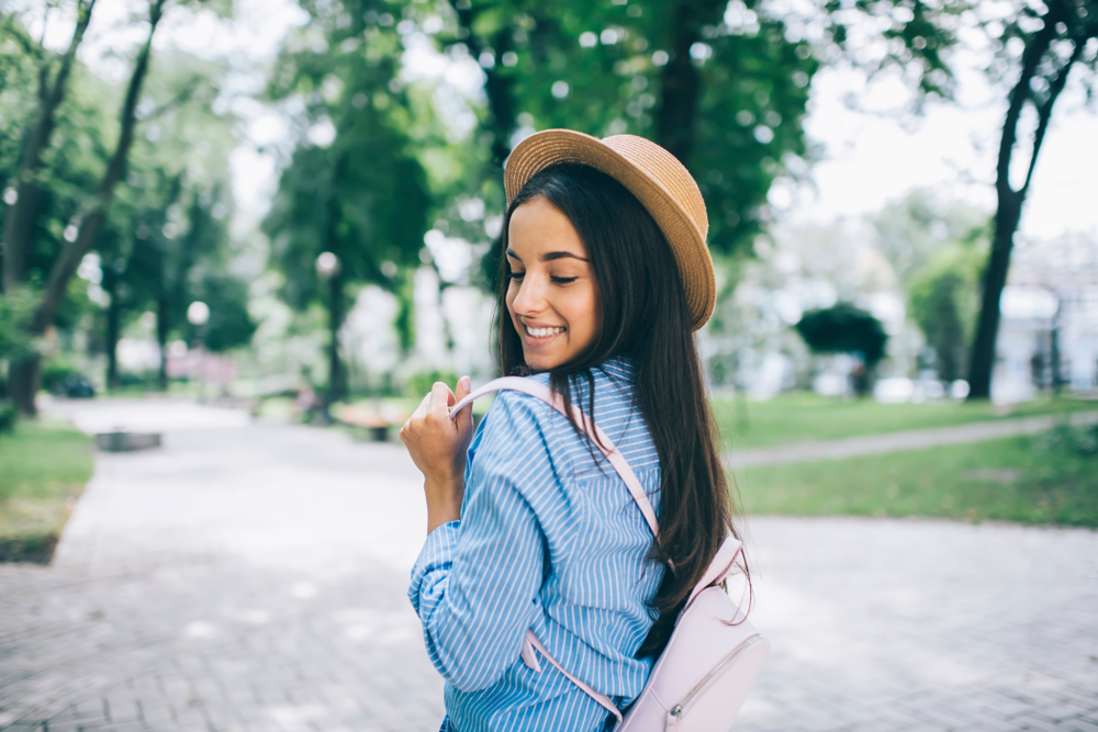 brunette wearing straw hat and small pink backpack