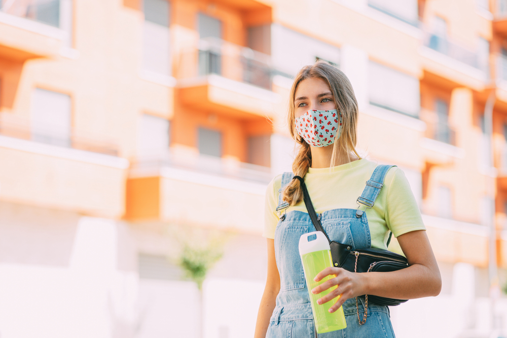 girl holding a water bottle as she's walking with a face mask on.