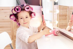 Young girl with hair in curlers smiling holding a makeup brush