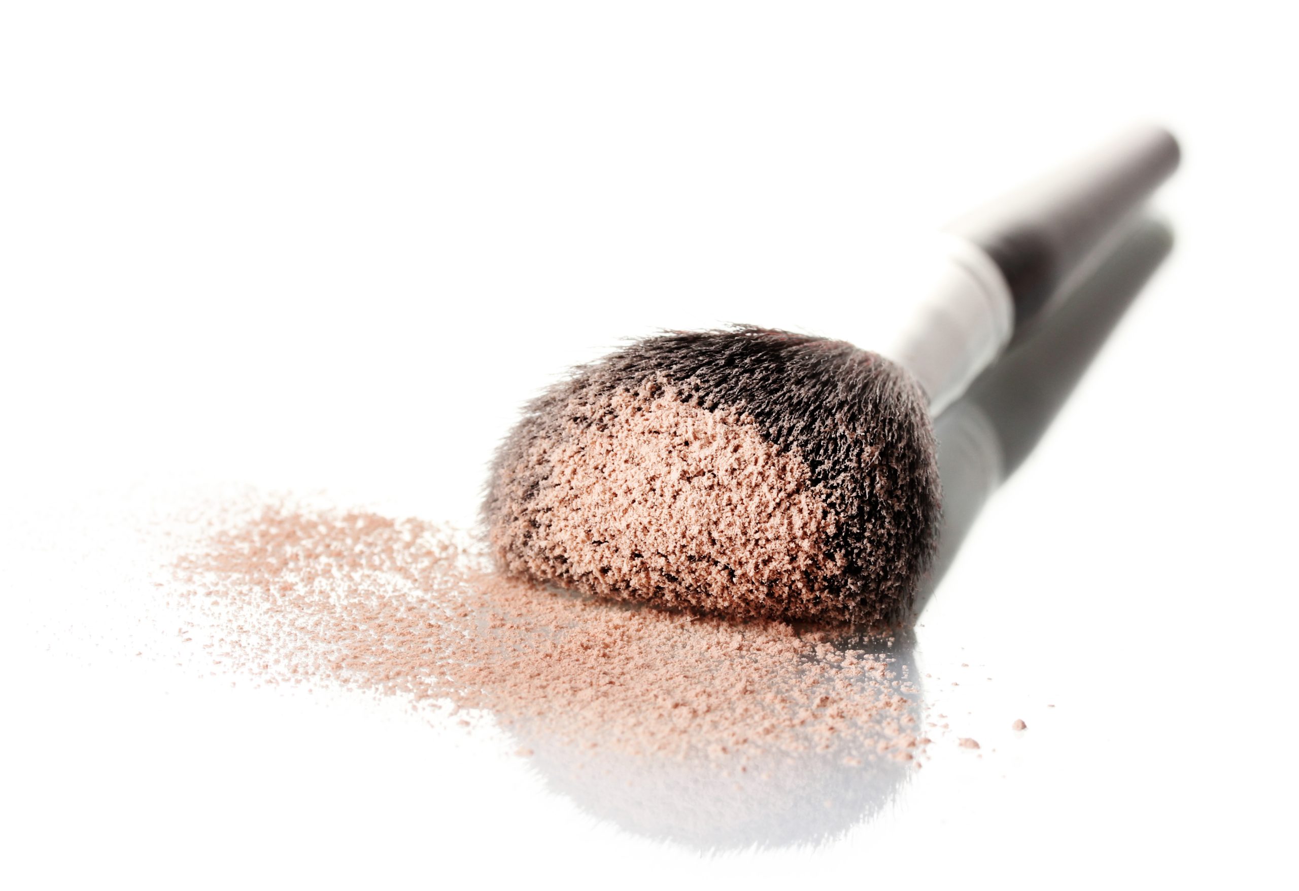 a powder brush laying on a table with a bunch of extra product on the brush and table